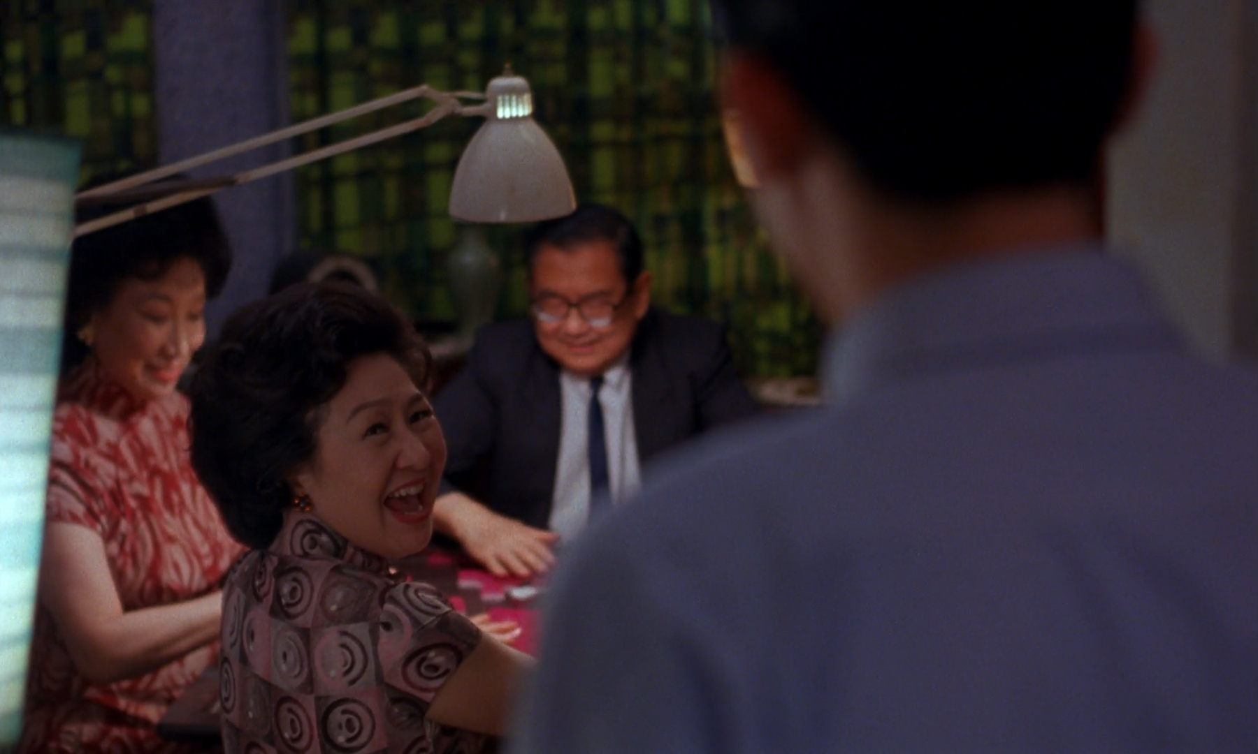 Guests sit around a banquet table while a woman in red and cream turns toward the camera.