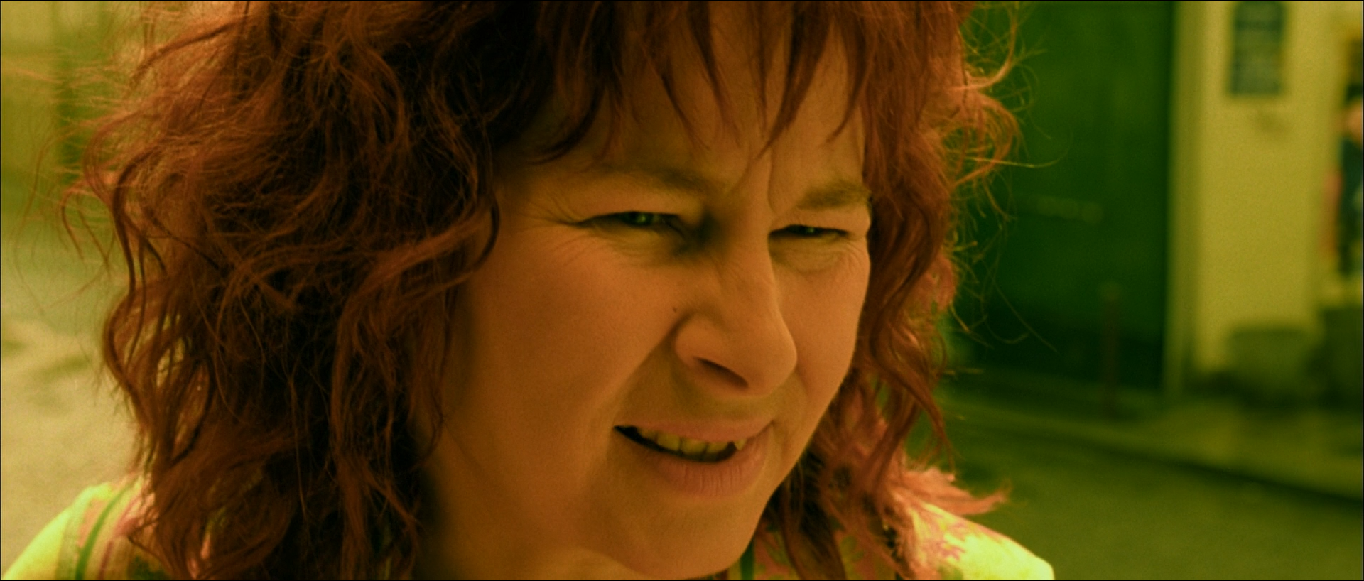 Close-up of a red-haired woman squinting in yellow-green light against a green interior.