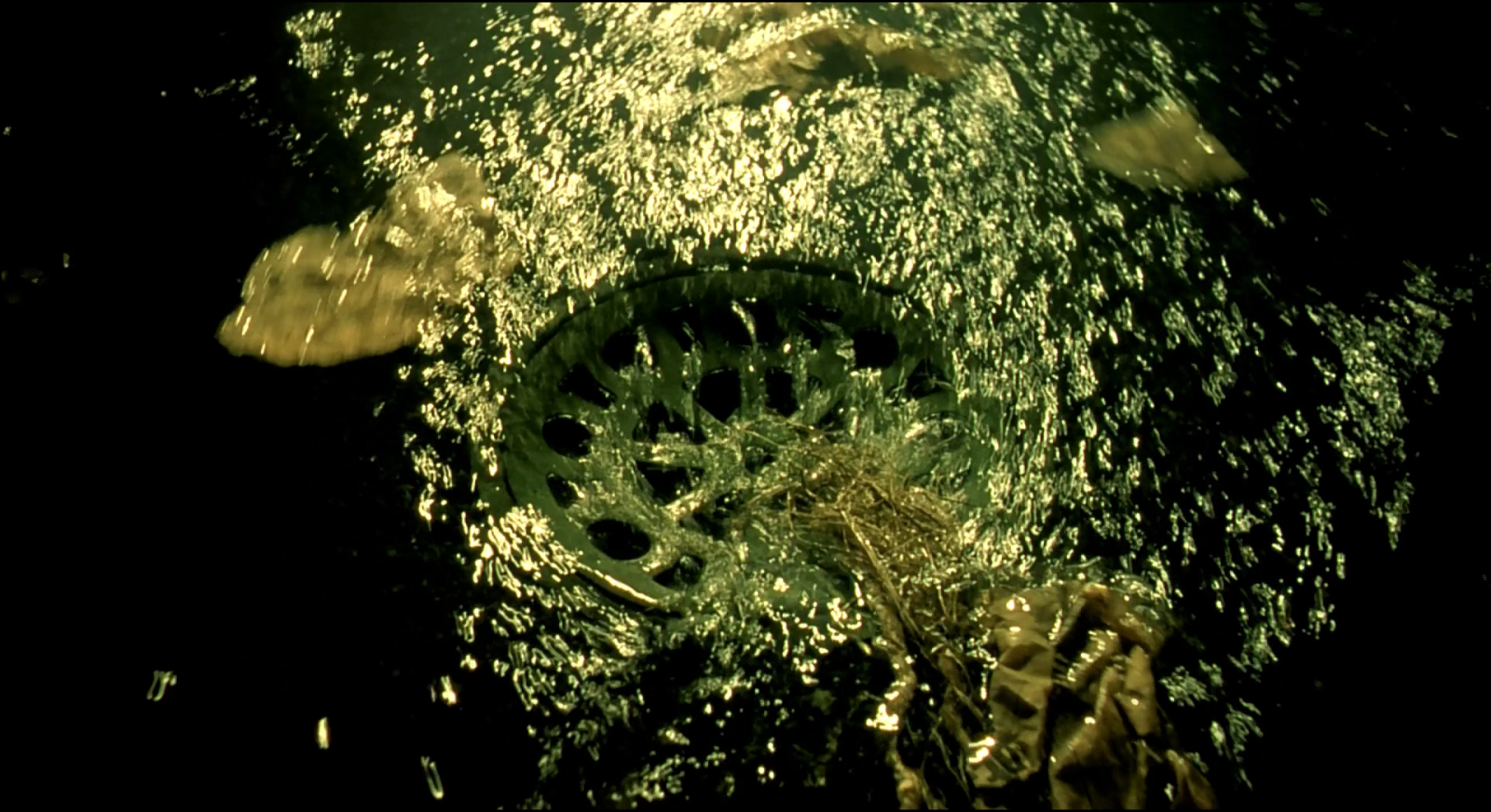 Water splashing over a metal drain, thousands of tiny gold-green specular highlights against black.