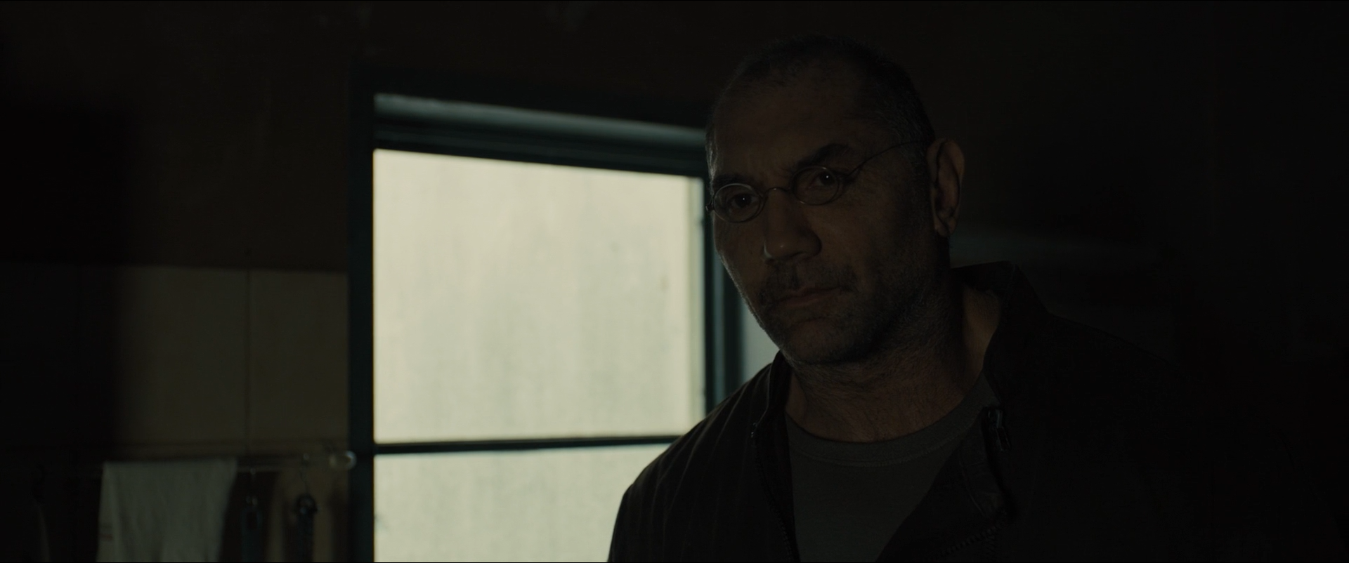 Shot 0039 from Blade Runner 2049 at 01:06:11:13. The window is allowed to clip to white while the room around it keeps almost no detail; the glasses, brow and shoulder emerge from that darkness by a narrow margin.