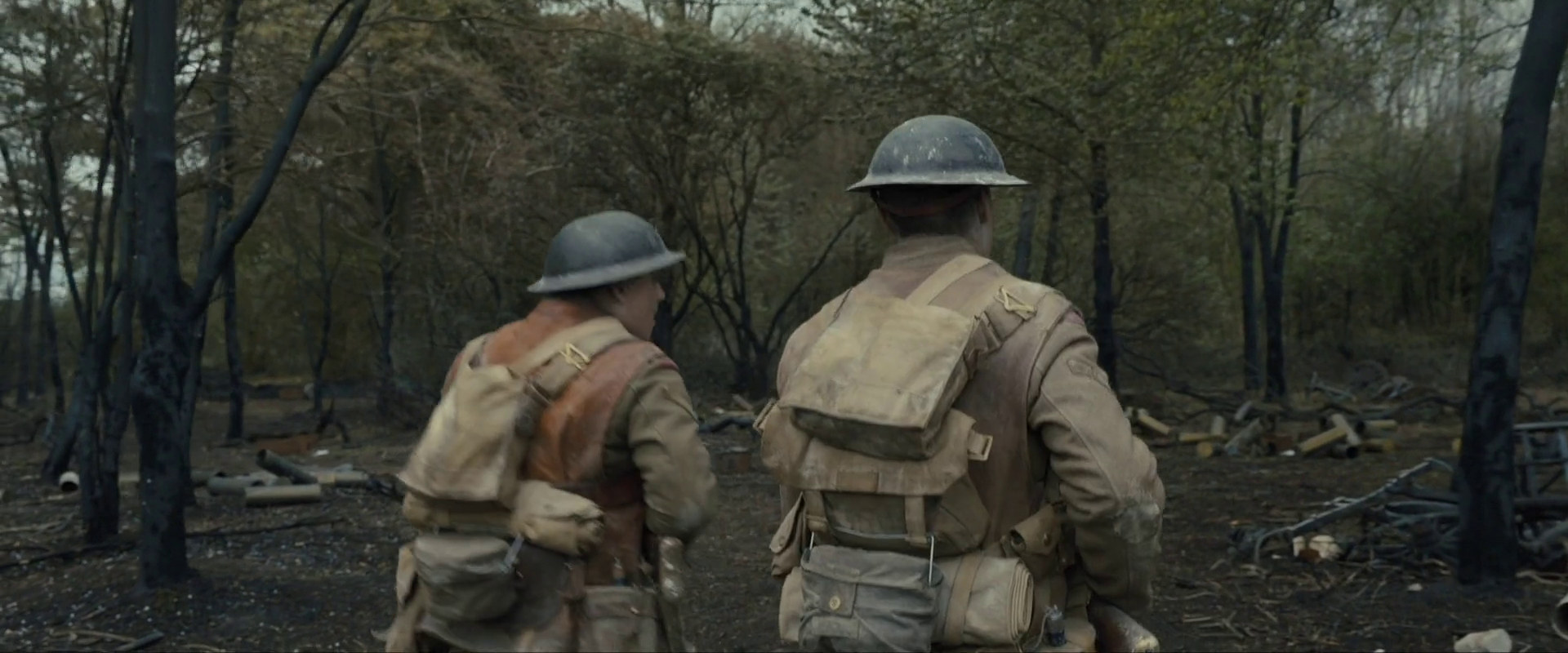 Sample 1052 from 1917 at 0:35:04. Charred trunks break the field into vertical black strokes; the men's khaki and webbing are the warmest notes, and the ground behind them stays grey throughout.