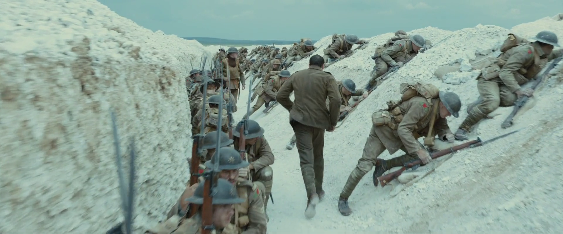 Sample 2852 from 1917 at 1:35:08. Cut chalk fills both sides of the trench and pushes the frame high and cool; the packed soldiers and their khaki are the only warm interruption in a white channel.