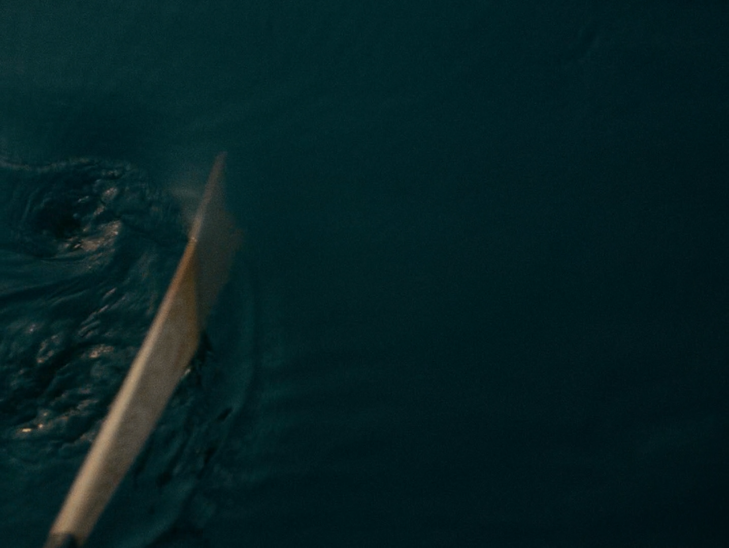 A paddle blade cutting a deep teal river surface seen from above.