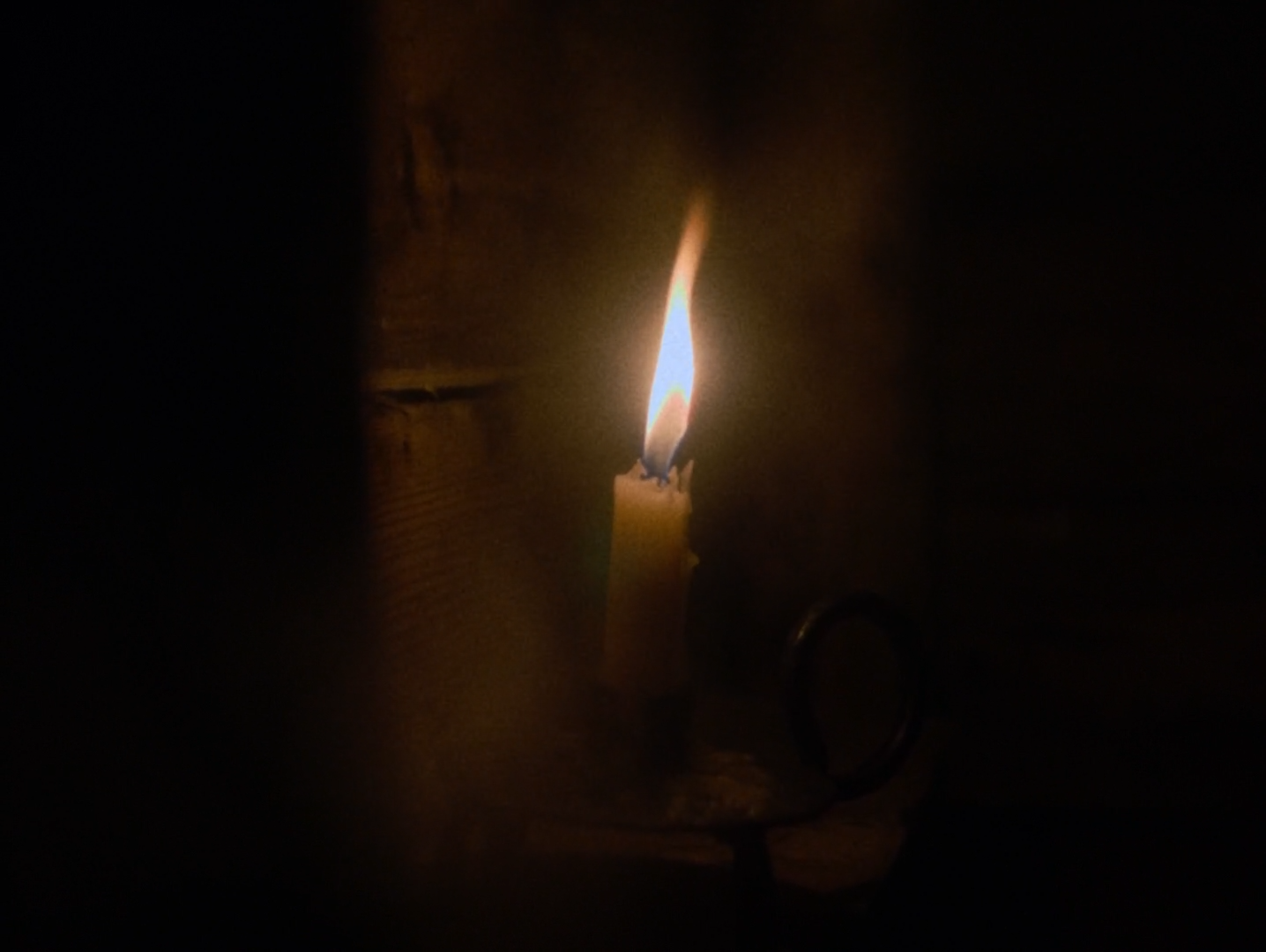 A single candle burning in an iron holder against dark vertical boards.
