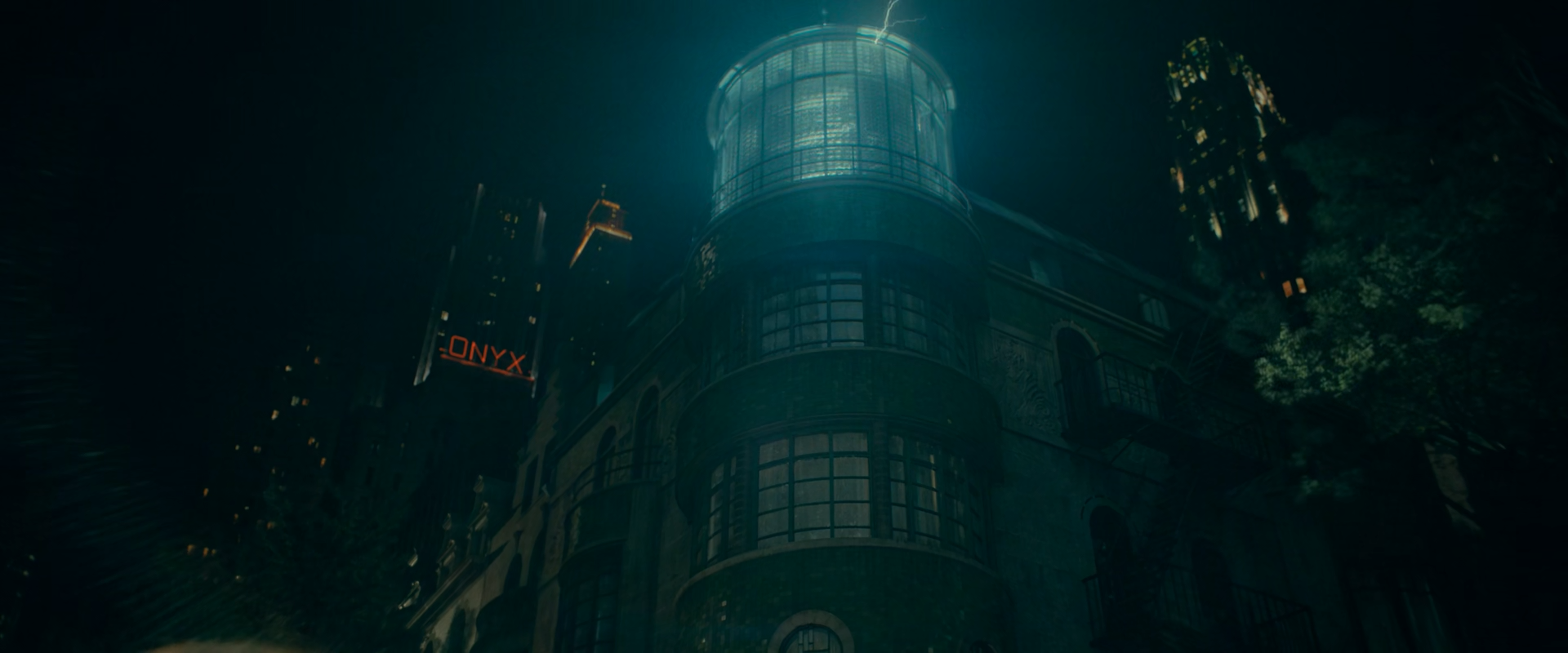 Low-angle night view of a rounded dark building topped by a glowing cyan glass tower with a small electrical spark above, surrounded by dark skyscrapers with scattered lit windows, an orange ONYX sign at left and trees at right.