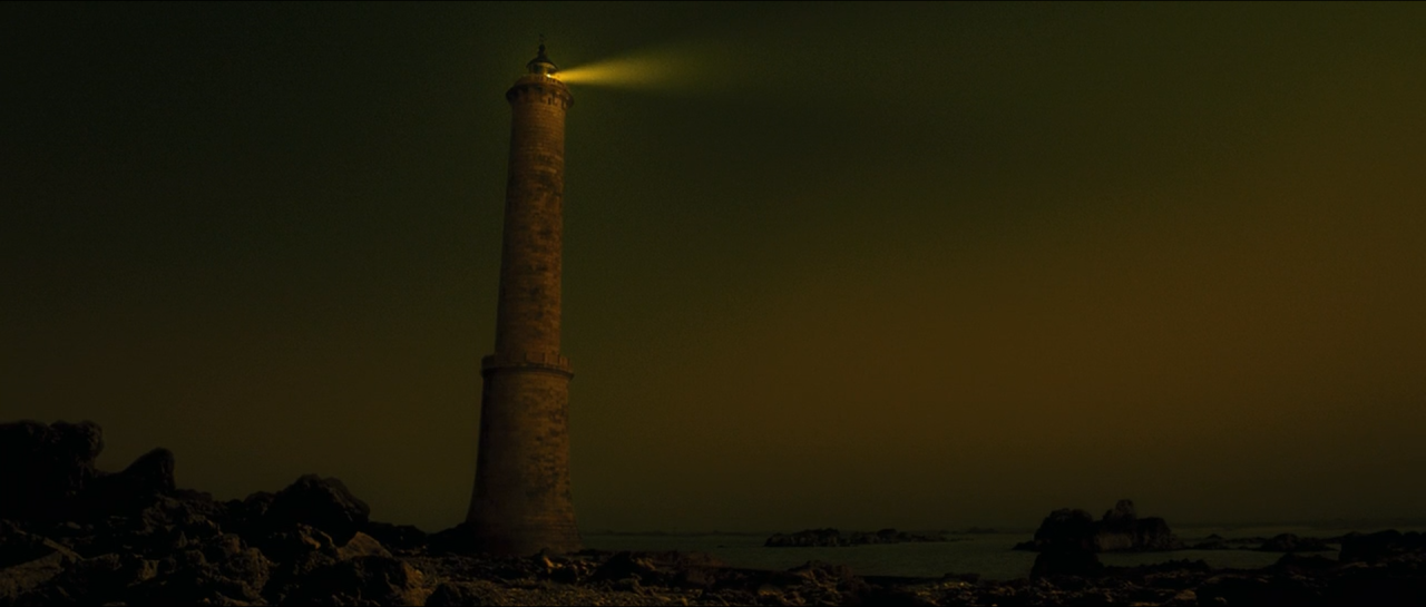 A solitary lighthouse tower against an extremely dark yellow-green horizon.