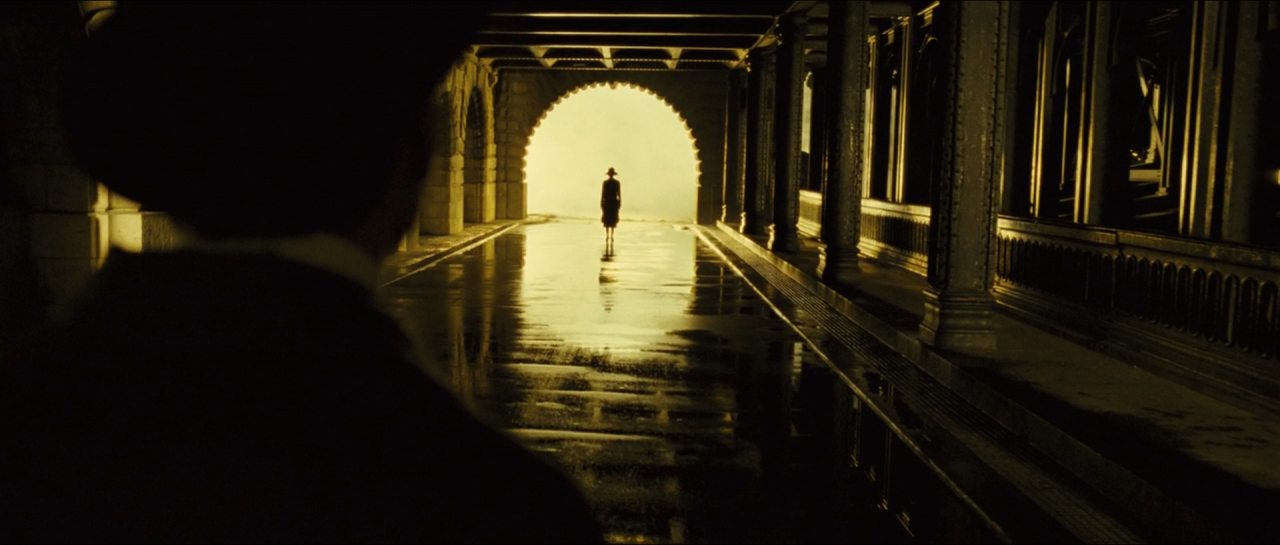 A tiny silhouetted figure in a bright doorway at the end of a dark golden corridor.