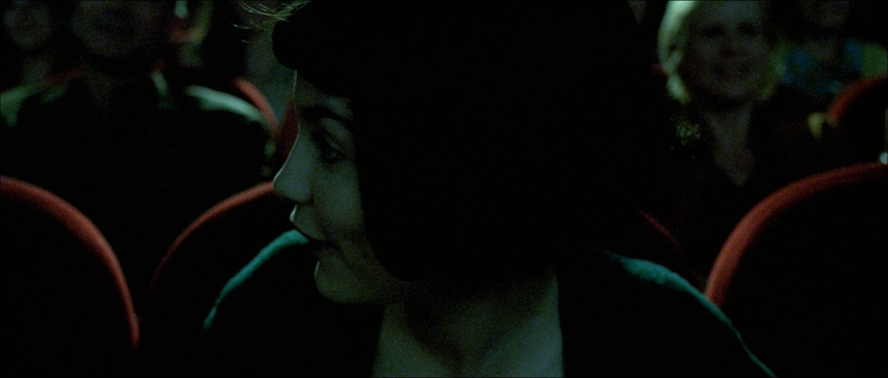 Two audience members barely illuminated among red cinema seats in green-black darkness.
