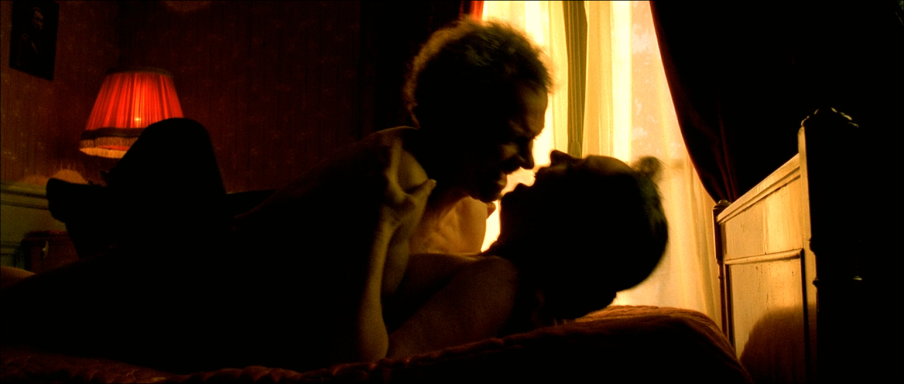 Two people in dark silhouette beside an intensely glowing bedroom curtain.
