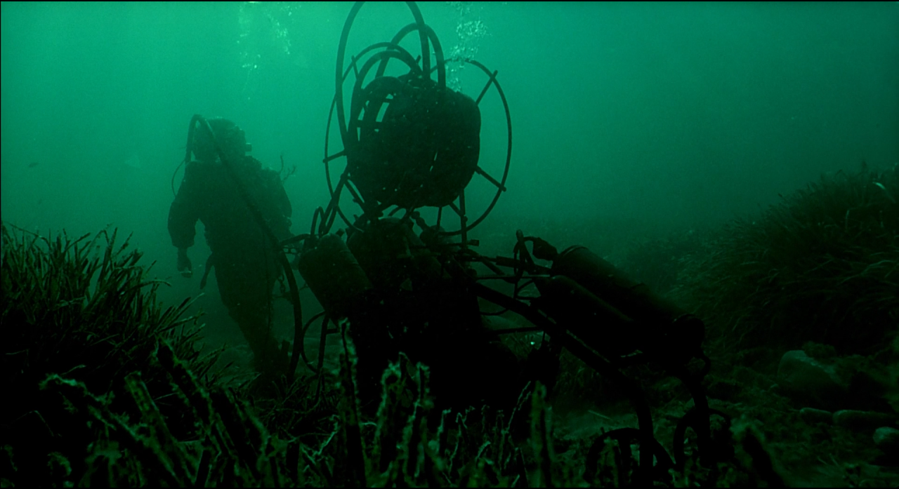 A diver and machinery in dark green underwater light.