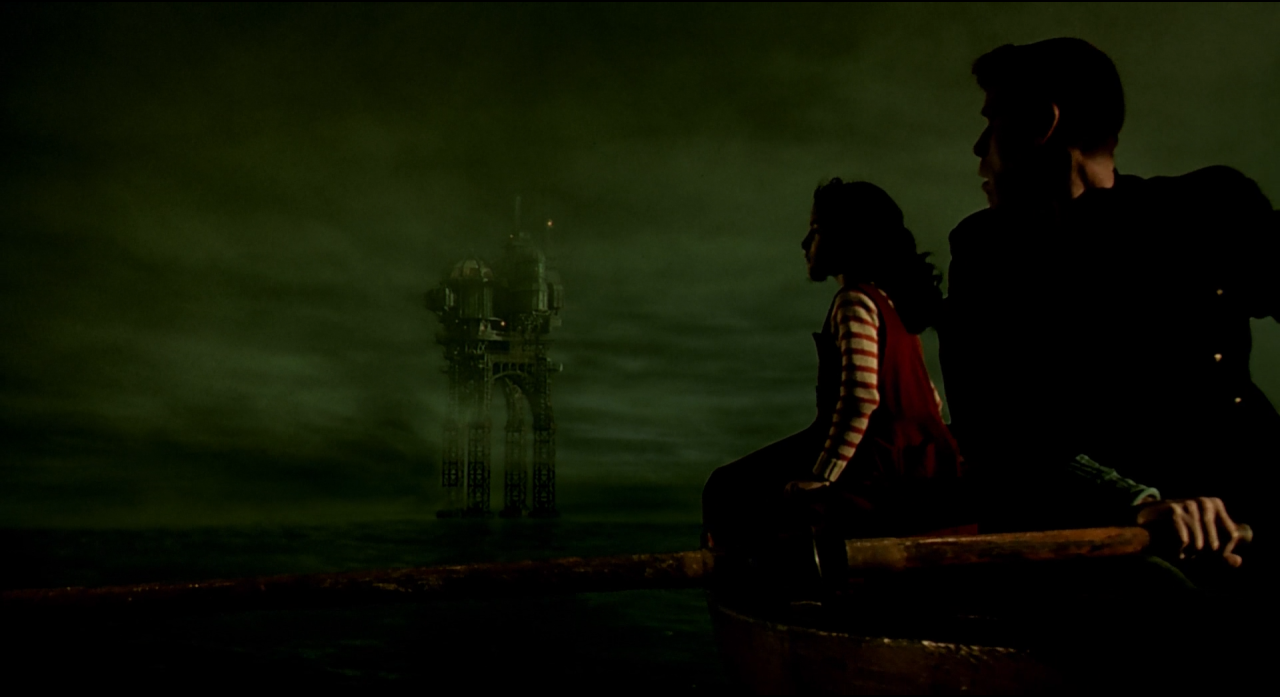 Two silhouetted figures seated before a distant green industrial landscape.