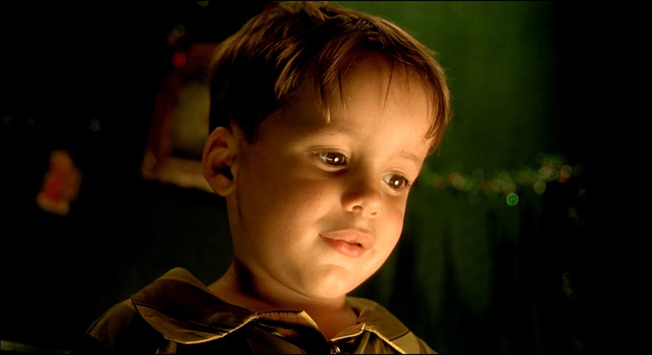 A child's face lit warmly from below against a dark green-black background.