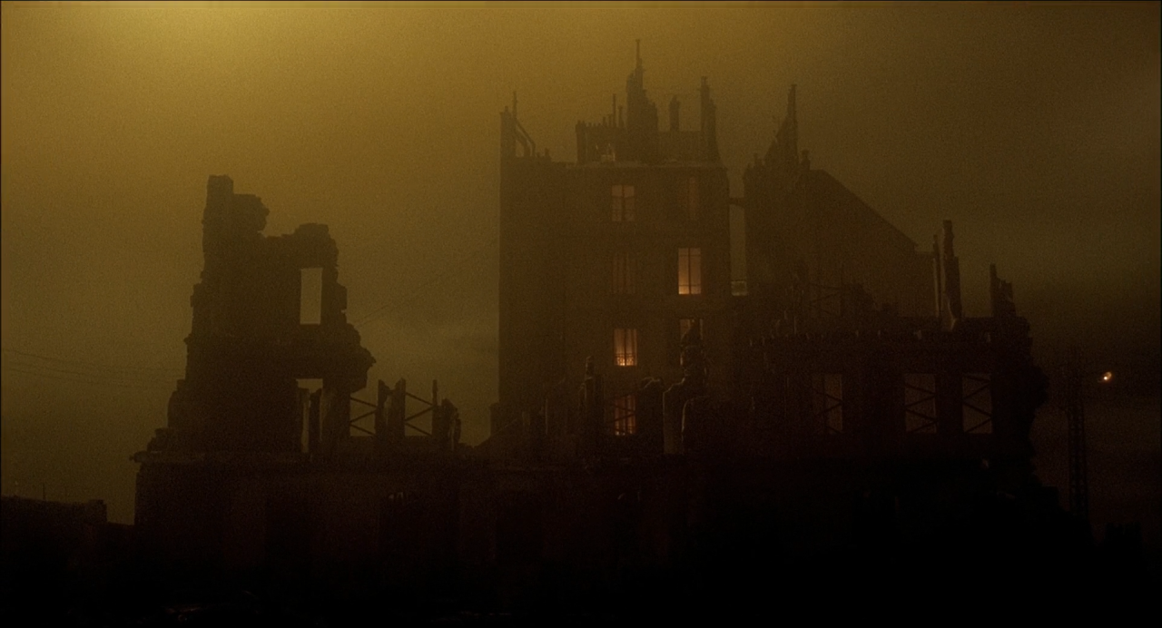 Dark ruined apartment buildings silhouetted in dense amber fog.