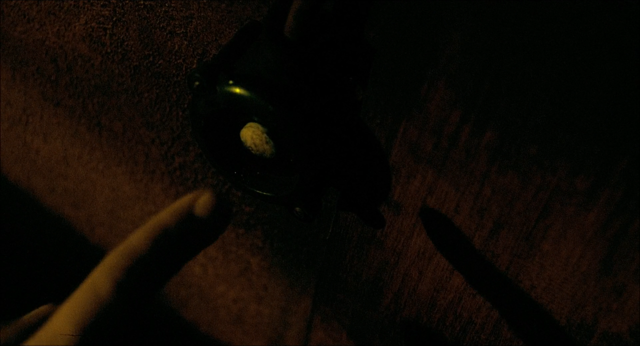 A finger points toward a tiny illuminated keyhole in an almost black wooden surface.