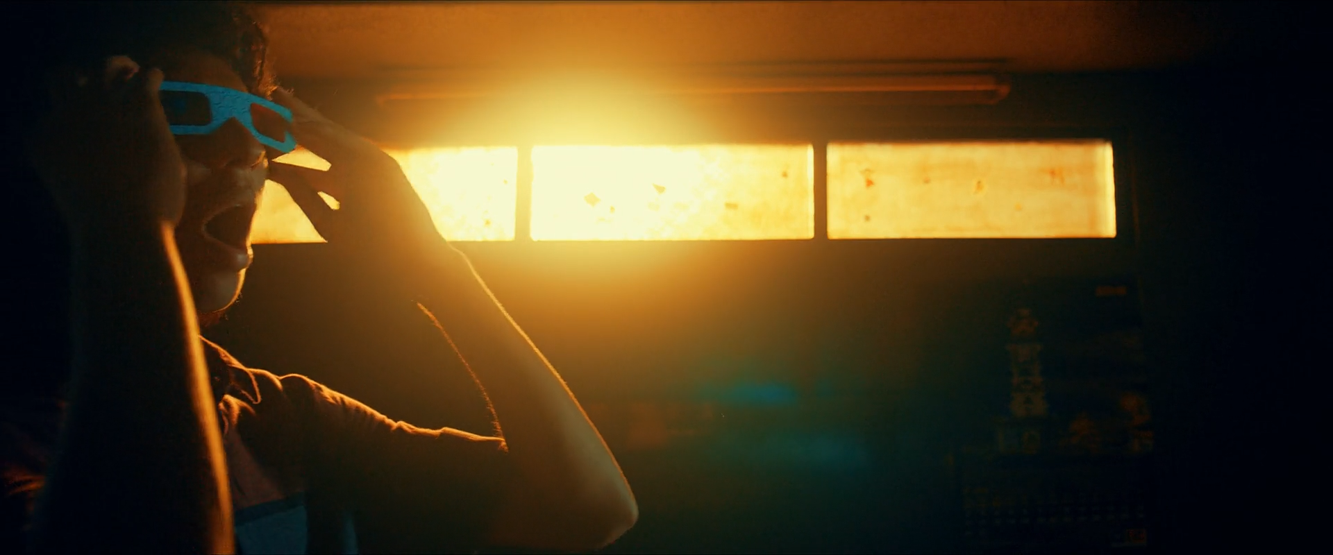 A dark figure wearing cyan 3D glasses stands between three glowing amber window panels in a flare-filled room.