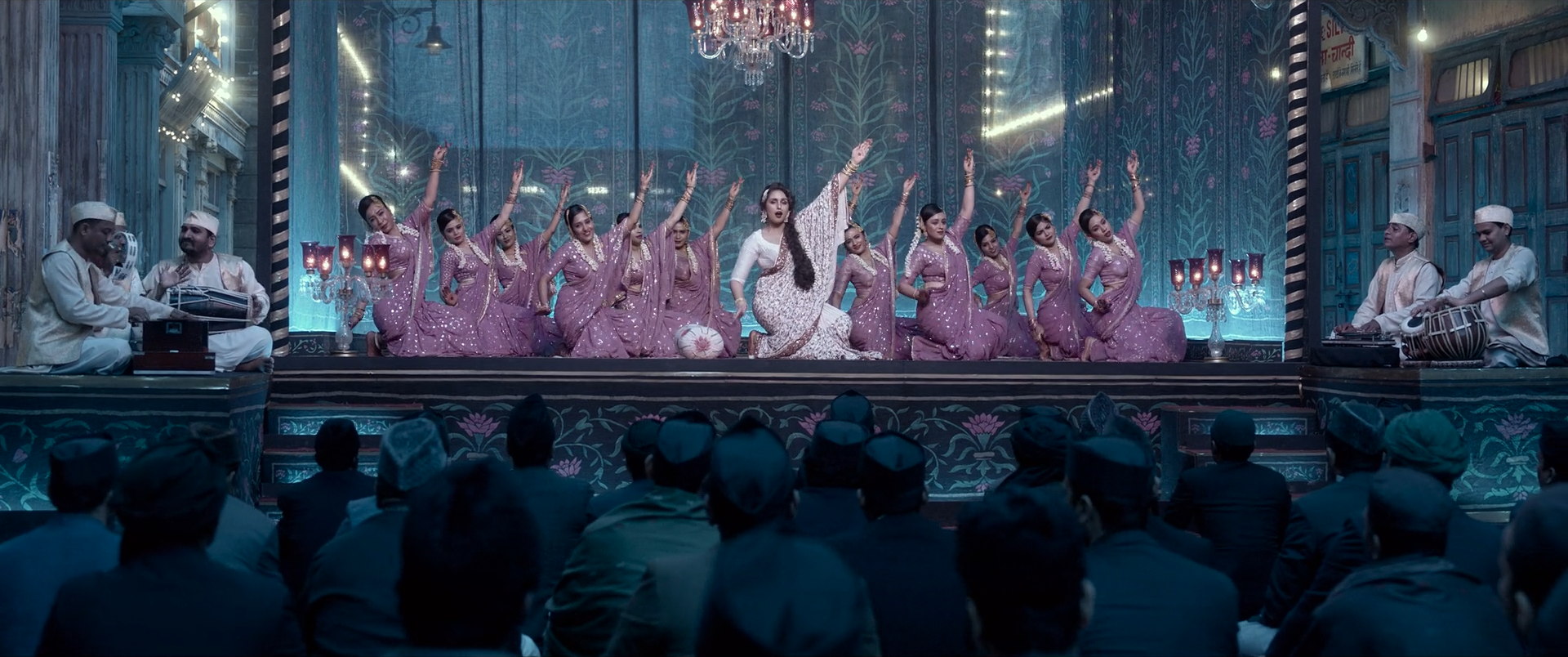 A symmetrical stage tableau with a white-clad lead, mauve chorus and architecture, and a cyan-blue audience beyond.